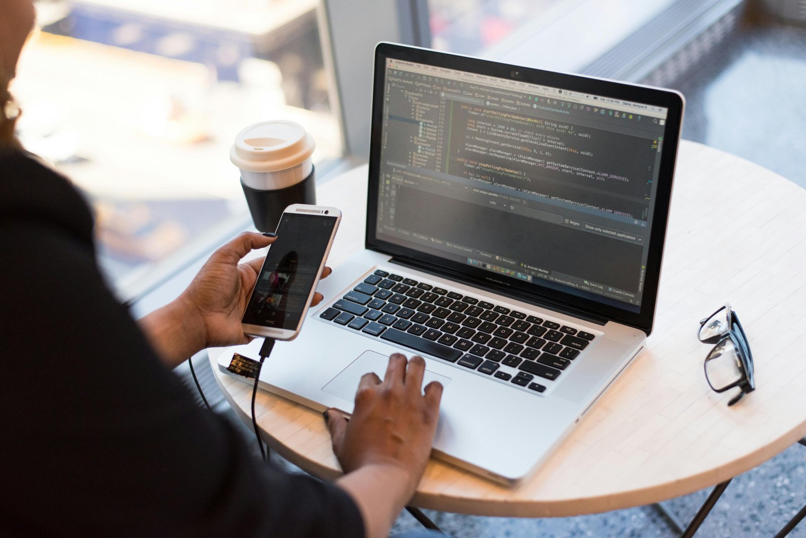 Home Developer working remotely, coding on a laptop with phone in hand, showcasing modern work culture.