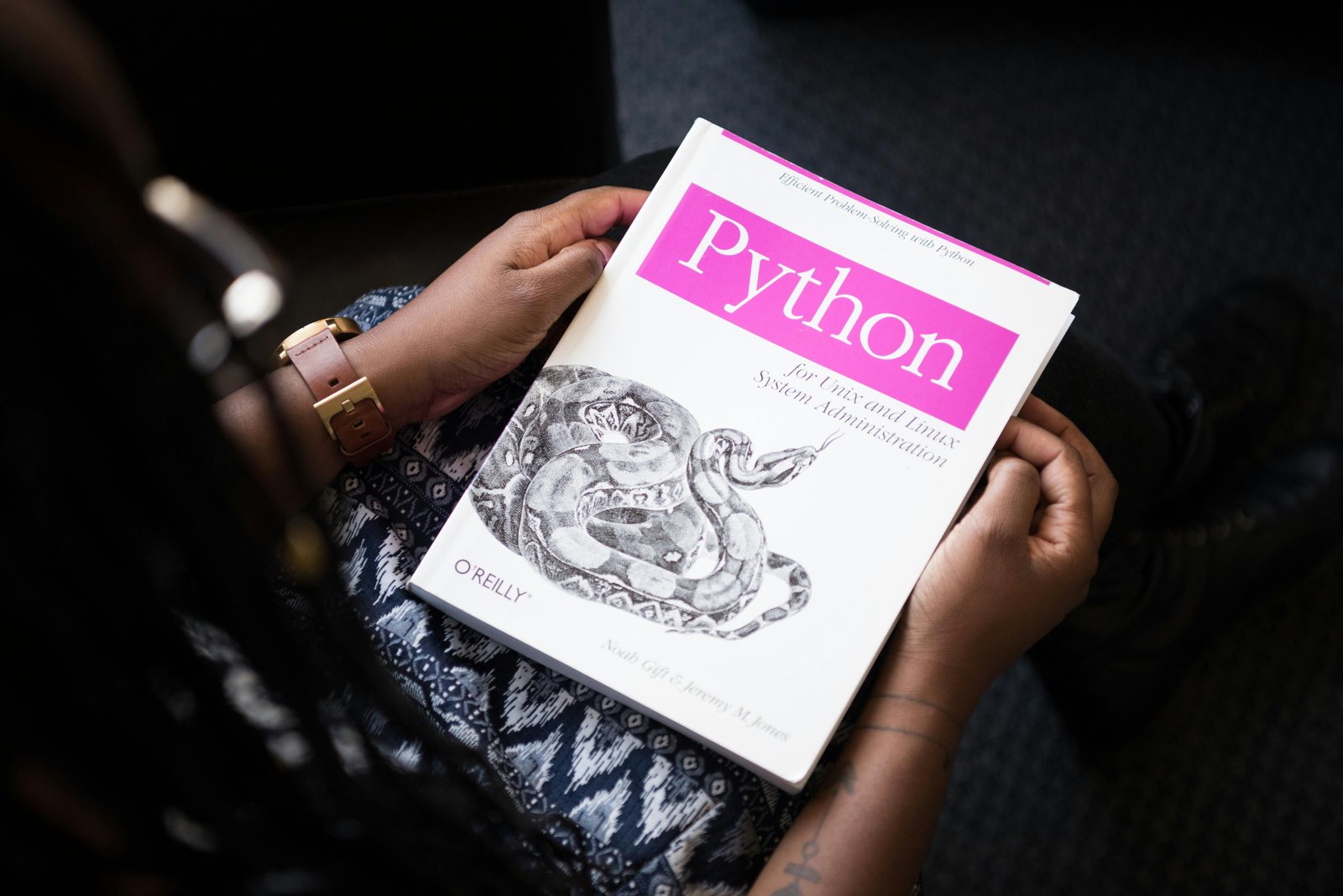 Home A person reads 'Python for Unix and Linux System Administration' indoors.